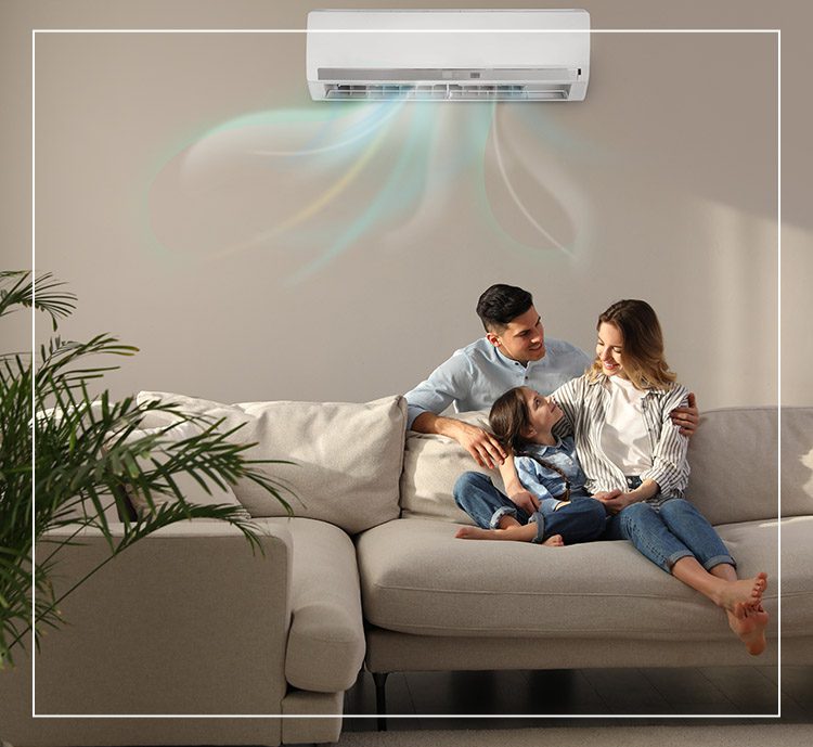 A family sitting on the couch under an air conditioner.