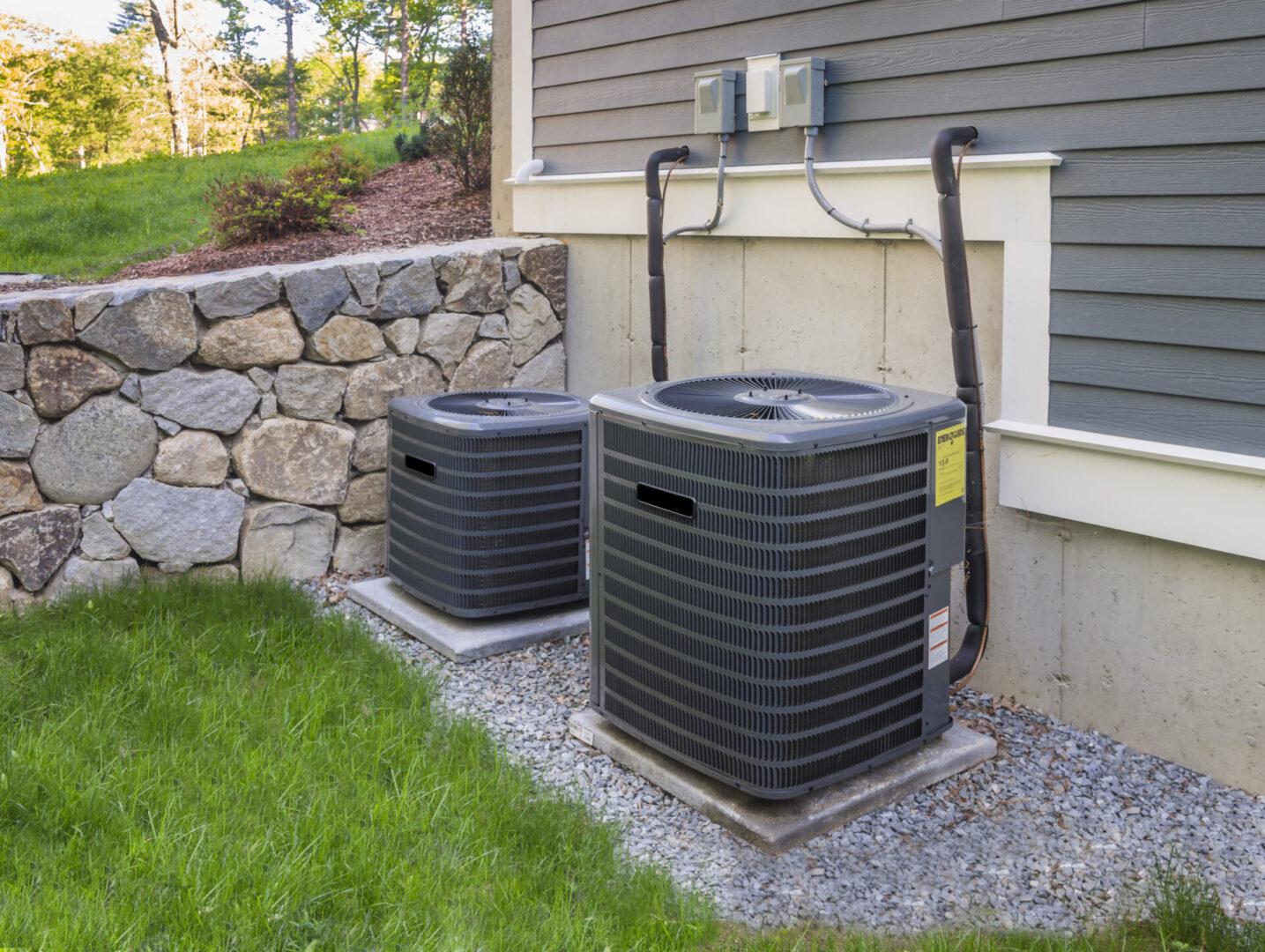 Two air conditioners are sitting outside of a house.