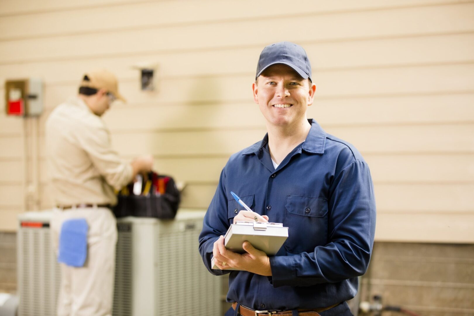 A man in blue shirt holding papers near an air conditioner.